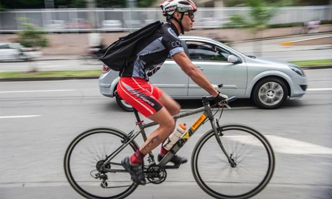 Pessoa andando de bicicleta em rua com carro branco ao lado