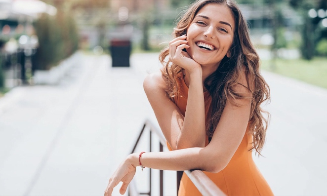 Mulher sorrindo usando roupas laranjadas e mão no queixo