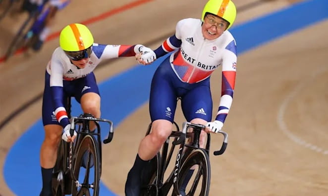 07 Madison Ciclista tocando a mão de outro em uma prova de madison