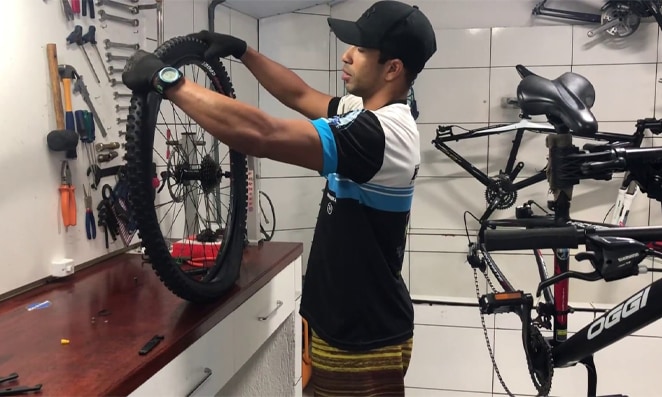 Pessoa segurando aro com pneu de bicicleta, ao fundo diversas ferramentas