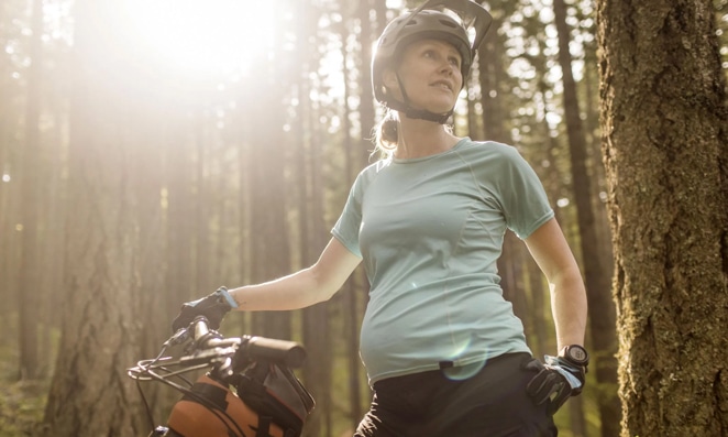 vista de uma gestante ciclista com sua bike em uma trilha na floresta
