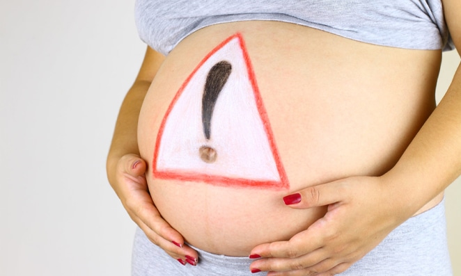 vista de frente da barriga de uma gestante com um sinal de aviso desenhado em sua barriga