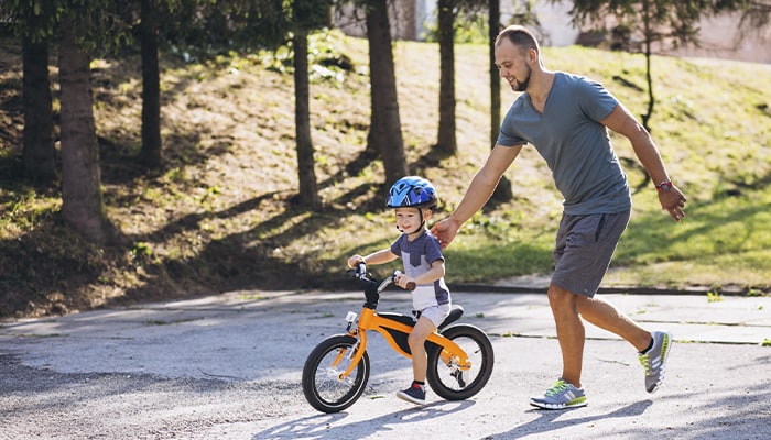 Pai empurrando a bicicleta de seu filho que está começando a andar de bike