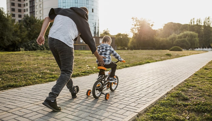 Pai empurrando a criança andando de bike com rodinha